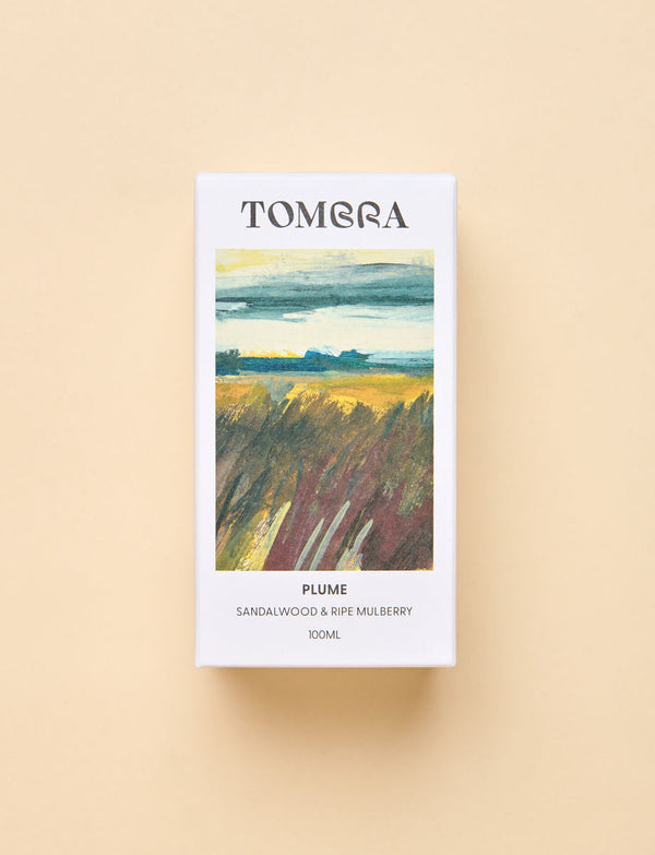 A rectangular Tomara fragrance box labeled 'PLUME' with a landscape-style painting on the front, photographed against a warm beige background.