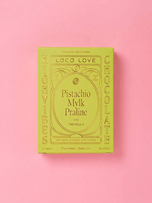 A rectangular box of Loco Love Pistachio Milk Praline chocolate, featuring a light olive green cover with gold decorative text and border details, set against a solid pink background.