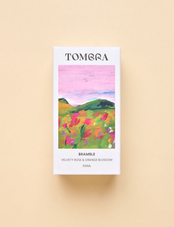 A rectangular Tombra fragrance box for Bramble, featuring a colourful watercolour-style landscape of pink sky and green hills, set against a solid beige background.