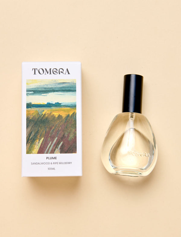 A Tombra room spray bottle with a black cap and clear glass, shown next to its white packaging box featuring a landscape painting on a beige background.